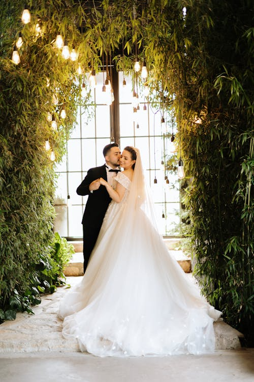 Bride and groom posing under warm hanging lights in a lush green garden setting