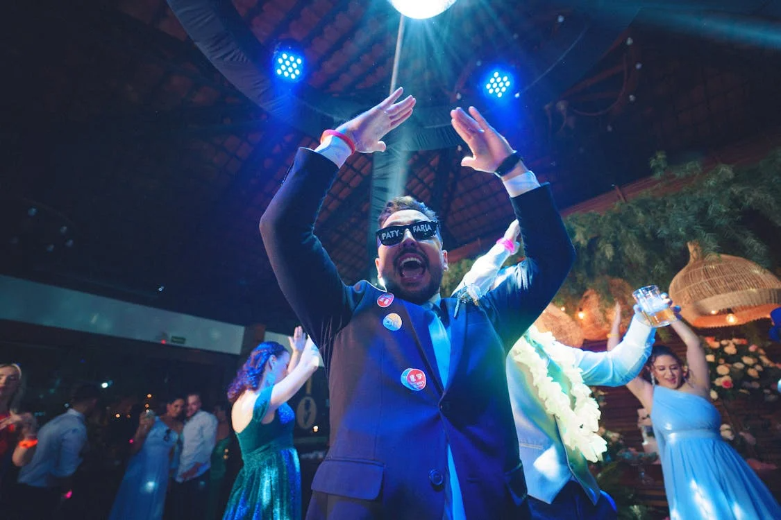 a man celebrating and dancing in front of the camera wearing glasses at a wedding after party