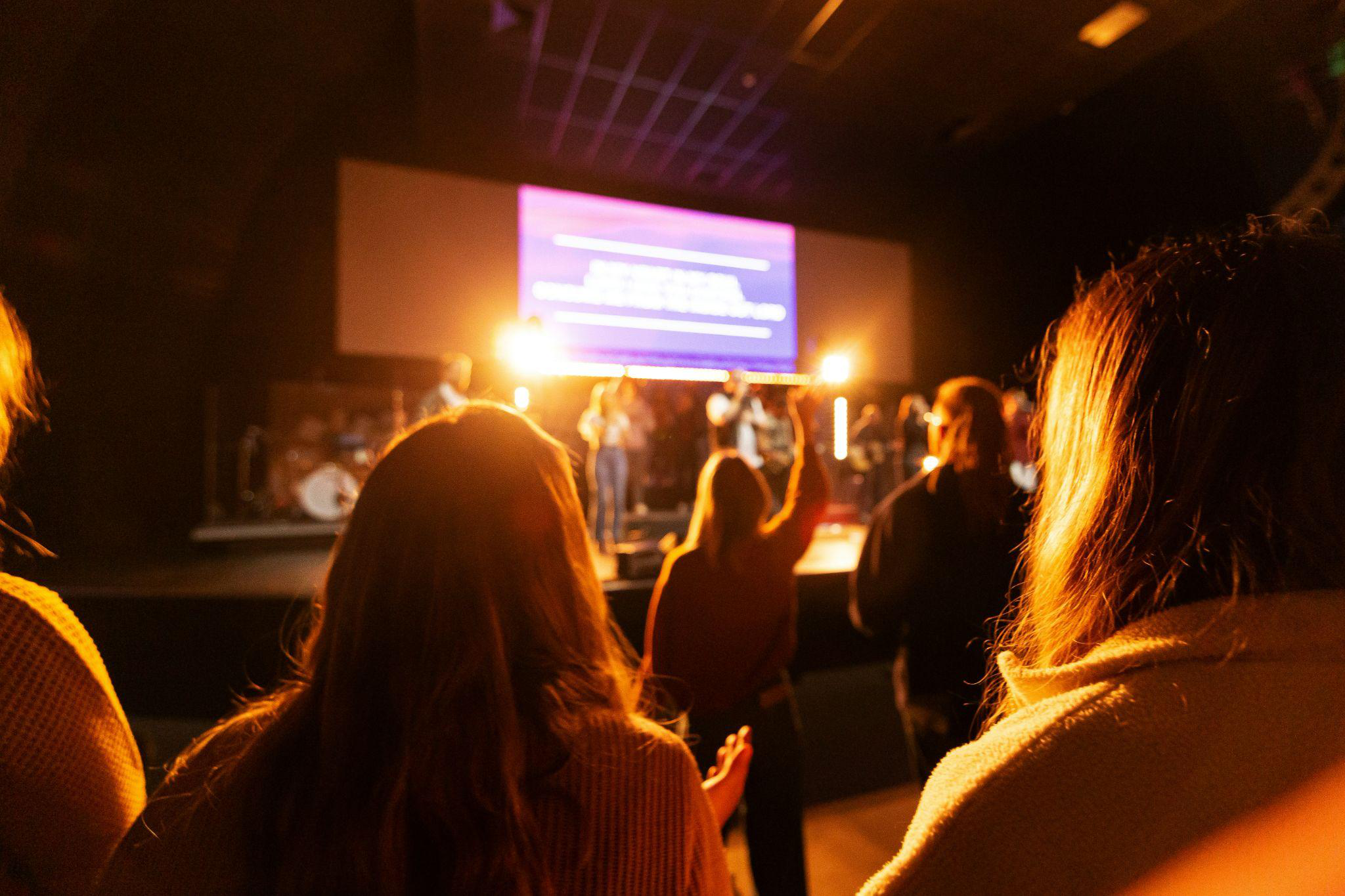 Audience looking up to a brightly lit presentation at an event